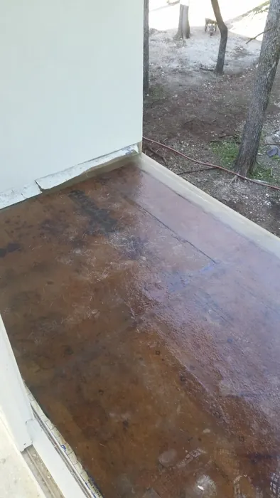 Exterior deck coated in waterproofing resin, membrane turned up the perimeter wall, wooded slope beyond