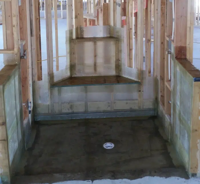 Head-on view of a shower under construction, resin membrane formed over the pan, curb, bench and stepped alcove in one piece, drain centred